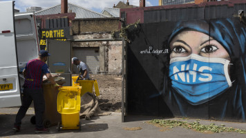 On the day that the UK death rate during the Coronavirus pandemic surpasses 40,000, including almost 10,000 care home residents, the highest rate in Europe, workmen clear a brownfield site next to a mural created by the anonymous street artist known as 'Artful Dodger' (after Charles Dickens's pickpocket character in Oliver Twist), of a Muslim NHS (National Heath Service) nurse wearing a surgical face mask, at Elephant & Castle in south London