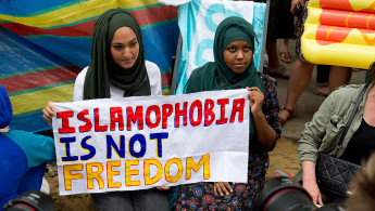 Two women in hijabs holding a sign reading "Islamophobia is not freedom"