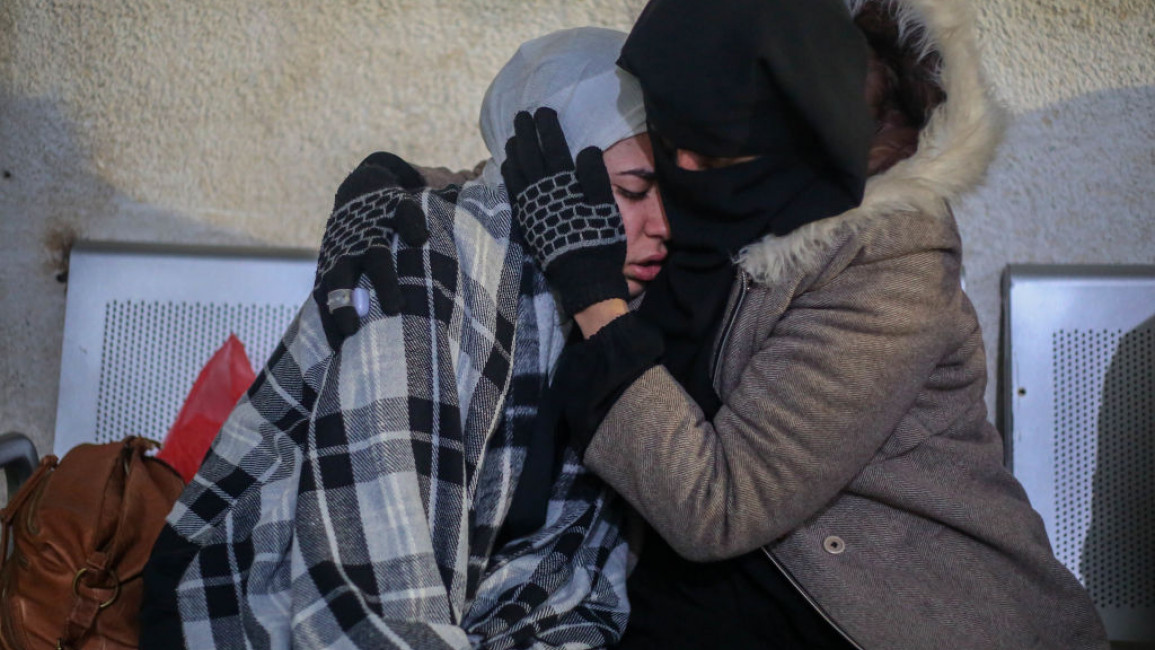 Two Palestinian women embrace. One appears visibly upset