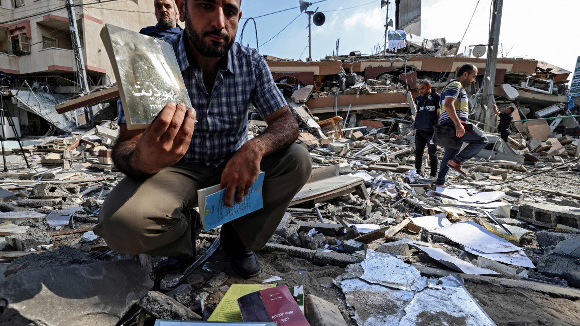 A Palestinian man holds books he picked up from amid the rubble of the Kuhail building [Getty]