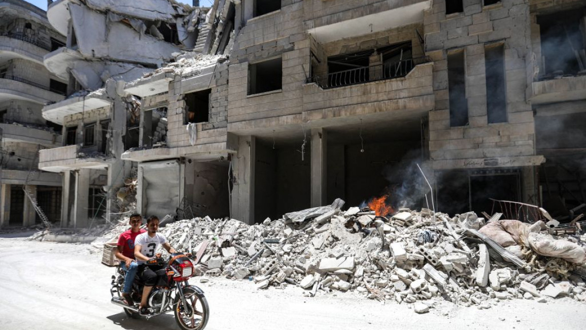 Men ride a motorcycle past debris outside a hospital damaged after a reported airstrike in Northeast Syria on 10 July, 2019. [Getty]