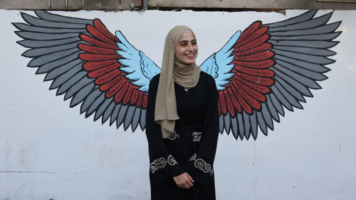 Palestinian activist Muna El-Kurd standing in front of a pair of wings on a wall