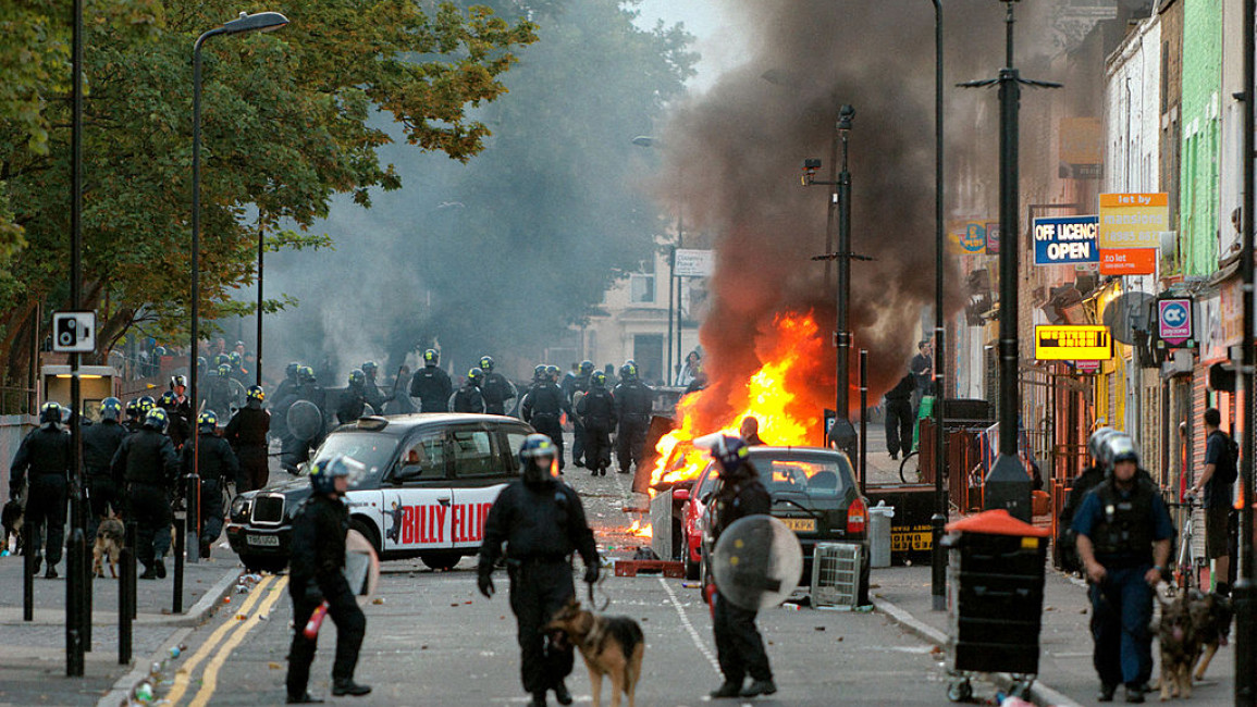 LONDON, ENGLAND - AUGUST 08: Riot police advance up Clarence Road as a car burns during clashes with rioters and looters in Hackney on August 8, 2011 in London, England. Pockets of rioting and looting continues to take place in various boroughs of London this evening, as well as in Birmingham, prompted by the initial rioting in Tottenham and then in Brixton on Sunday night. It has been announced that the Prime Minister David Cameron and his family are due to return home from their summer holiday in Tuscany,