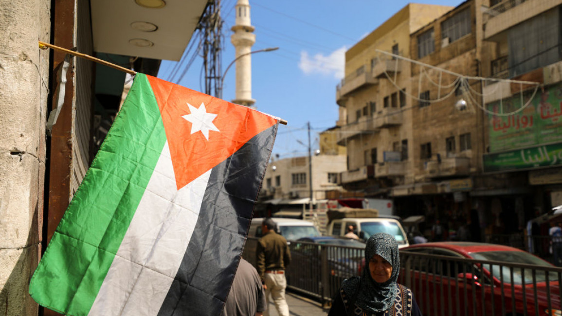 An elderly woman wearing a national headscarf walks past the national flag of Jordan on a shopping street in Amman. Jordan