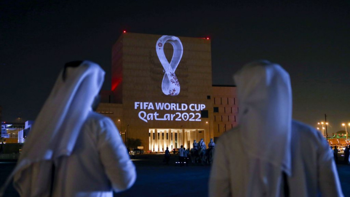 Two men look at the Qatar World Cup logo projected onto a building