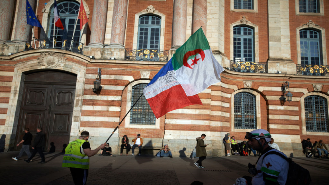 A Yellow Vest demonstrator walks near the townhall of Toulouse, the Capitole, with a French and an Algerian flag