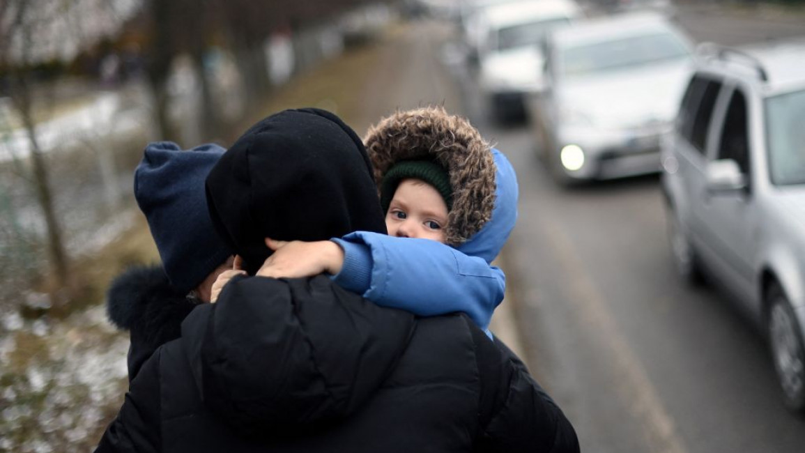 A child hugs his parents on the side of the road as cars queue on their way to the Medyka-Shehyni border crossing between Ukraine and Poland