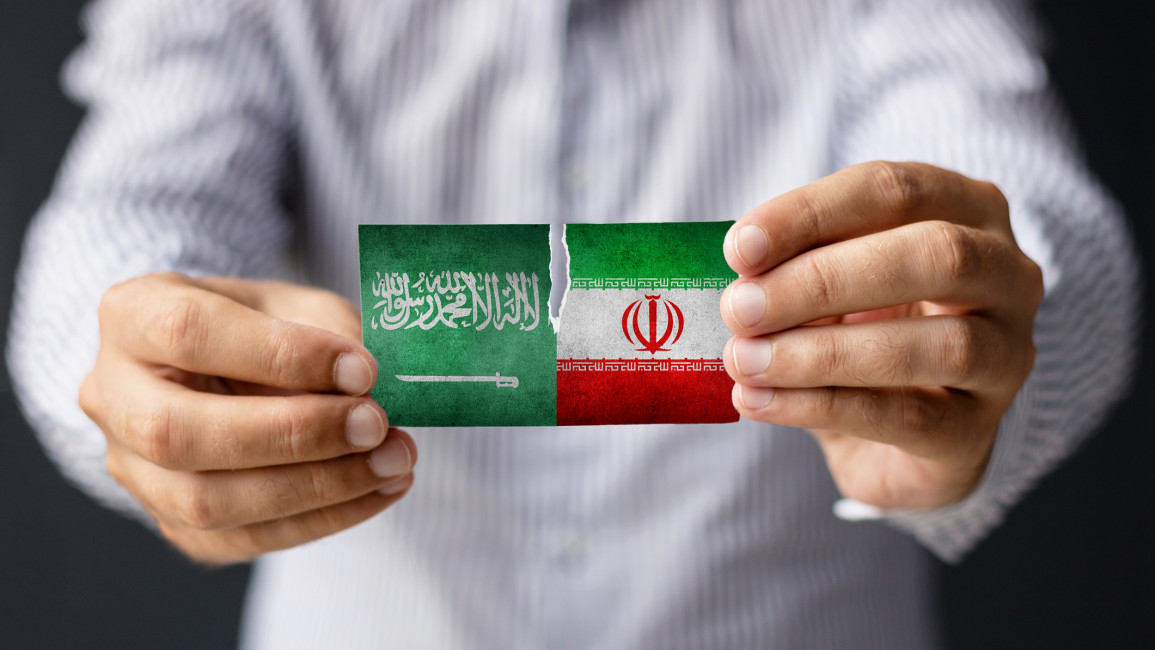 A man holding small Saudi and Iranian flags in his hands, side by side