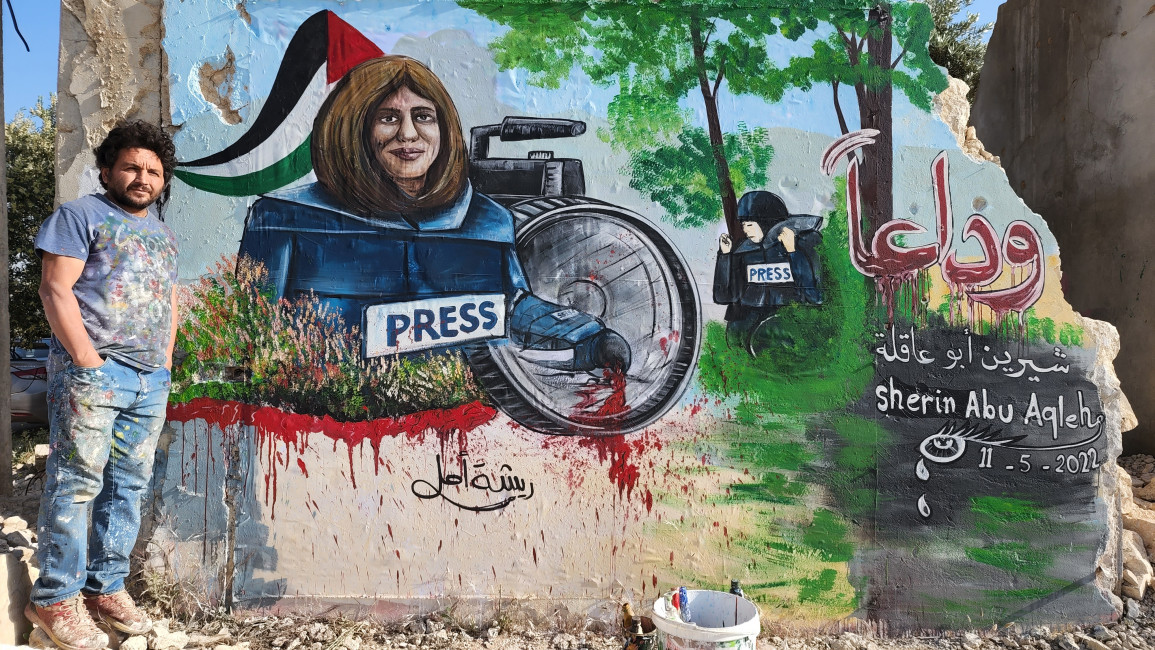 A mural of slain Palestinian journalist Shireen Abu Akleh. Syrian artist Aziz Al-Asmar stands to the mural's left.