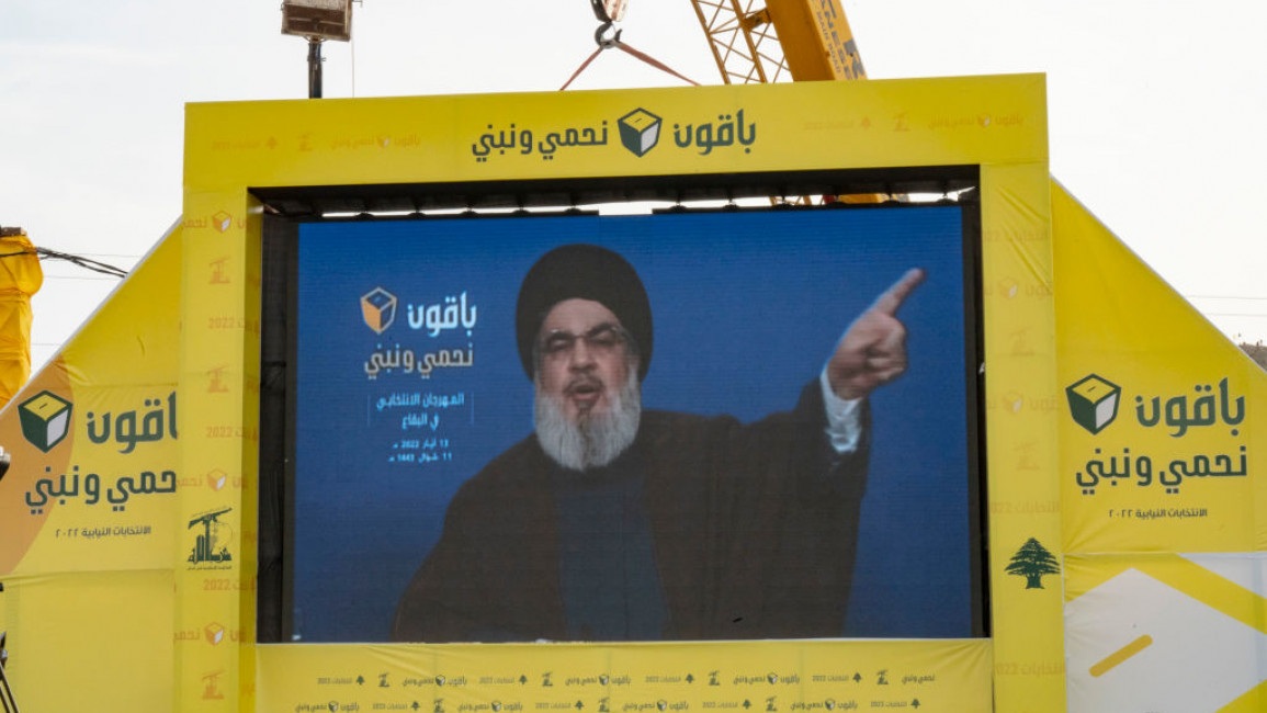 Hassan Nasrallah depicted pointing upwards and to his left on a large screen.