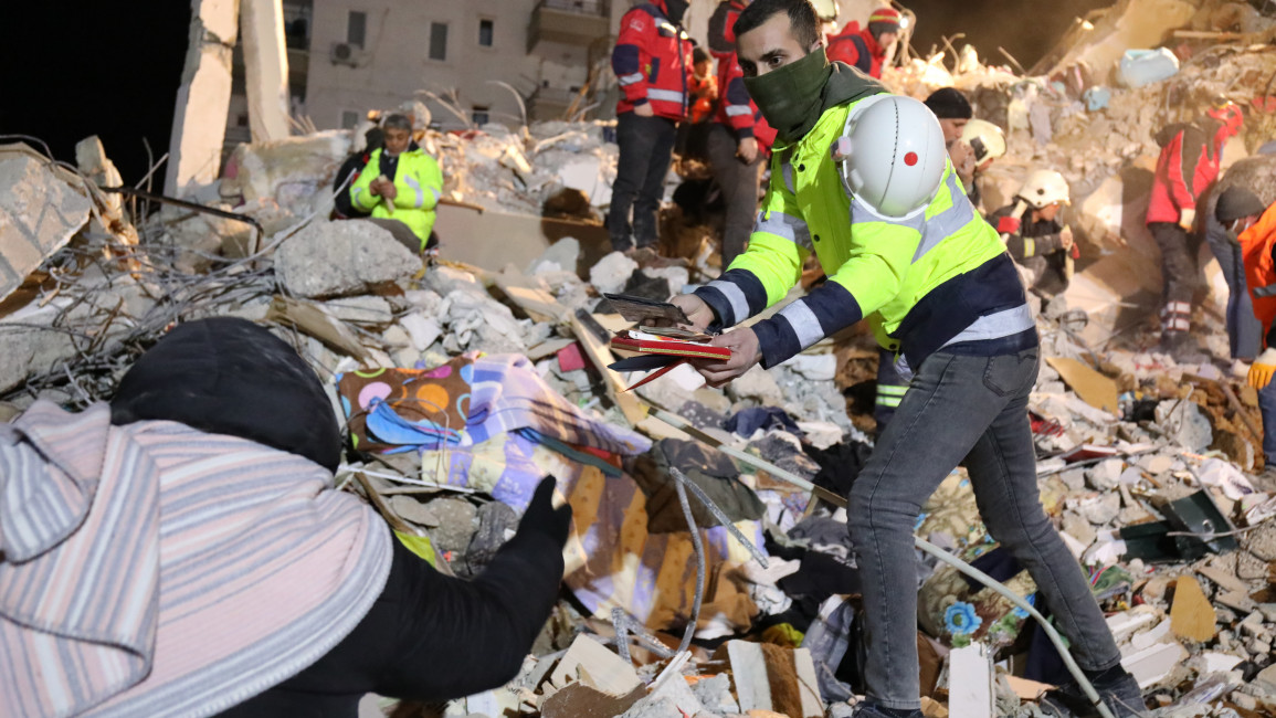 An aid worker hands the personal affects from a collapsed apartment building in Adana, Turkey to relatives waiting to see if their family members are still among those trapped in the rubble. [William Christou – TNA]