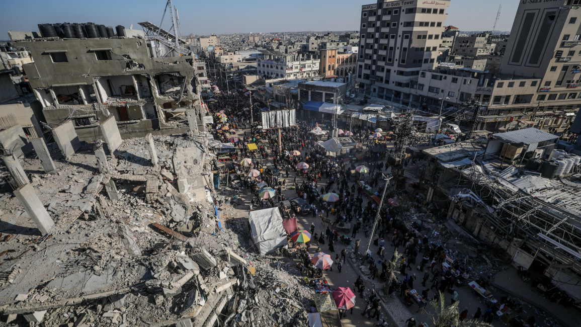  Palestinians walk past kiosks set up next to destroyed buildings along a street, on the first day of Ramadan, in Al Nusairat refugee camp, Gaza Strip, 11 March 2024.
