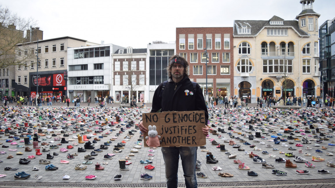 Man stands with a sign in front of a square full of shoes