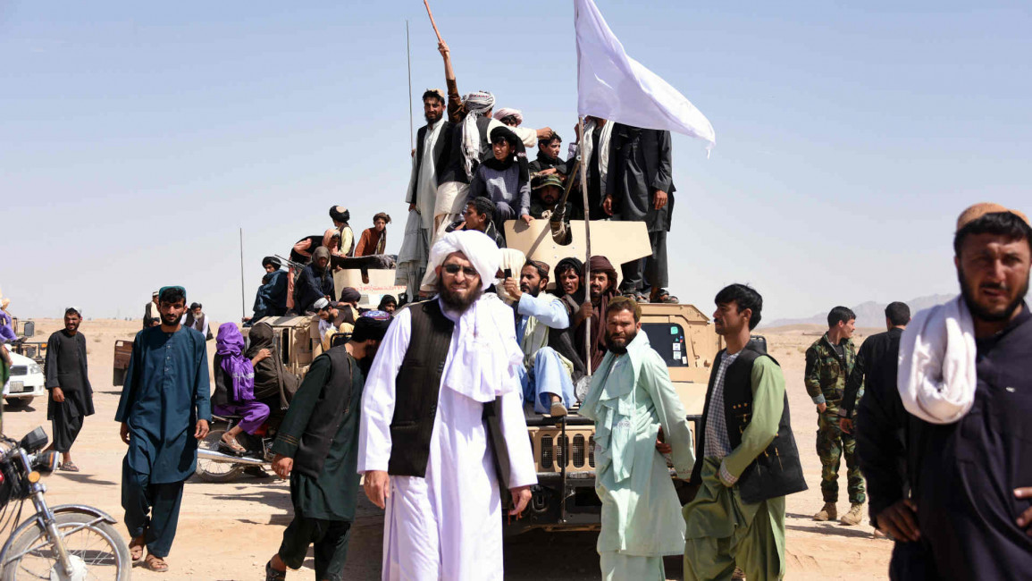 Taliban militants and residents stand on an armoured Humvee