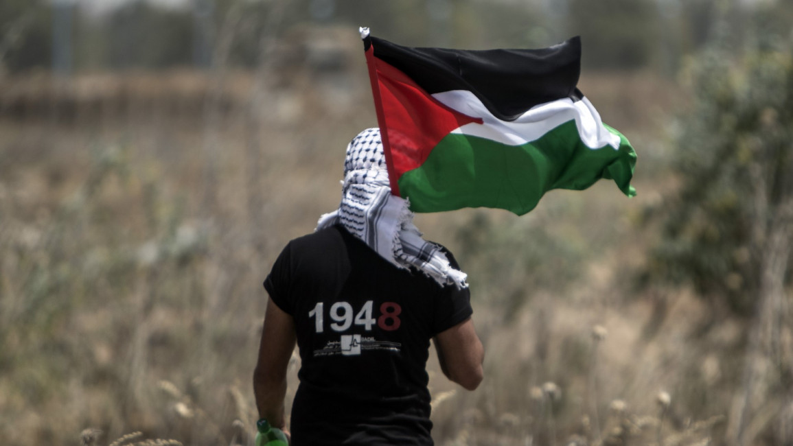 Palestinian youth waves national flag on Nakba anniversary. [Getty]