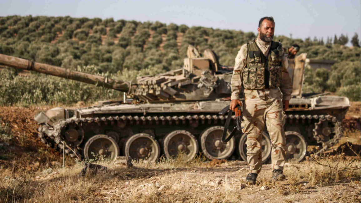 Syrian rebel fighter walks past tank