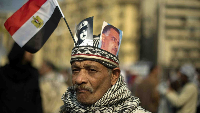 An anti-military rule protester wears a hat holding portraits of President Nasser December 2011